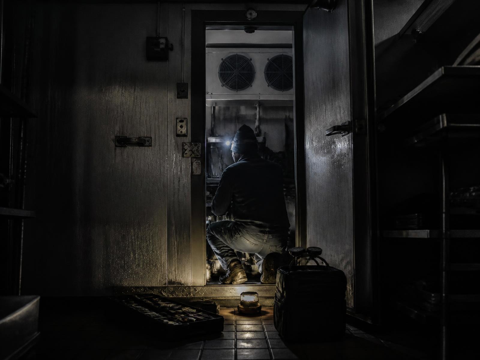 Refrigeration technician working inside an open walk-in cooler after hours